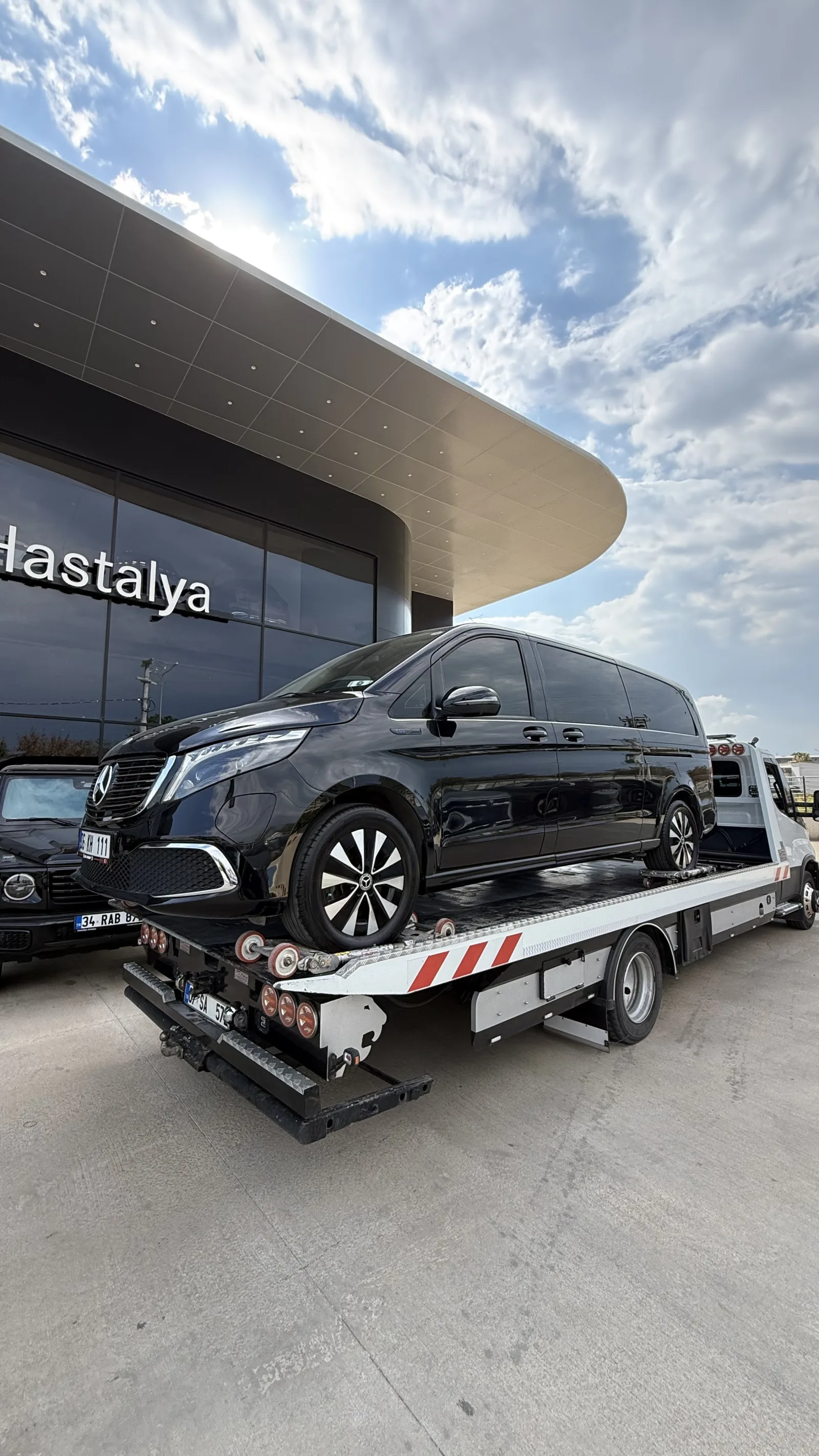 Otomotiv tesisi önünde platform çekici üzerindeki siyah minibüs