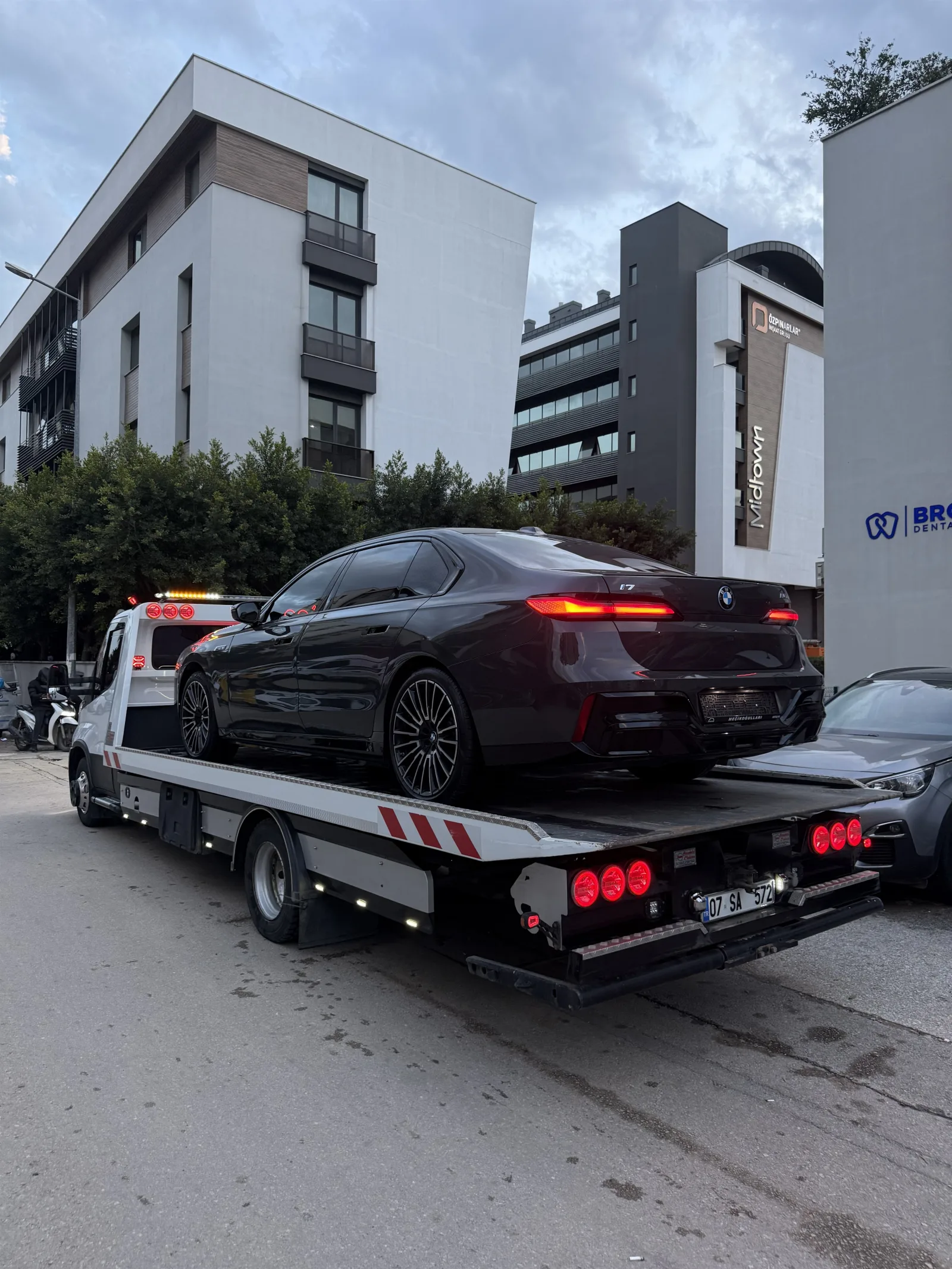 Şehir içinde platform çekici üzerinde taşınan siyah sedan, arkadan görünüm
